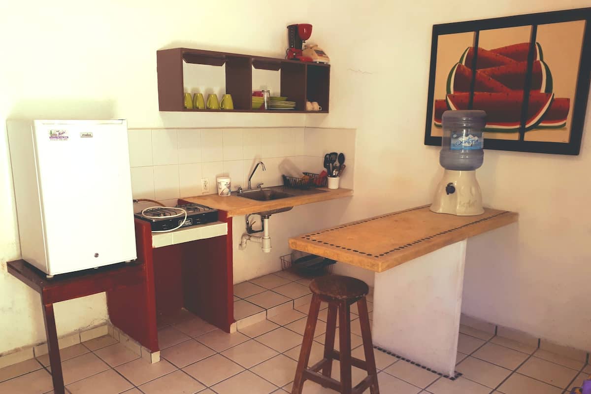 Cozinha compacta com geladeira, fogão, pia e um banquinho.