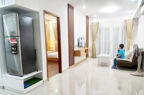 A modern hotel room with a refrigerator, a TV, a sofa, and a fan.