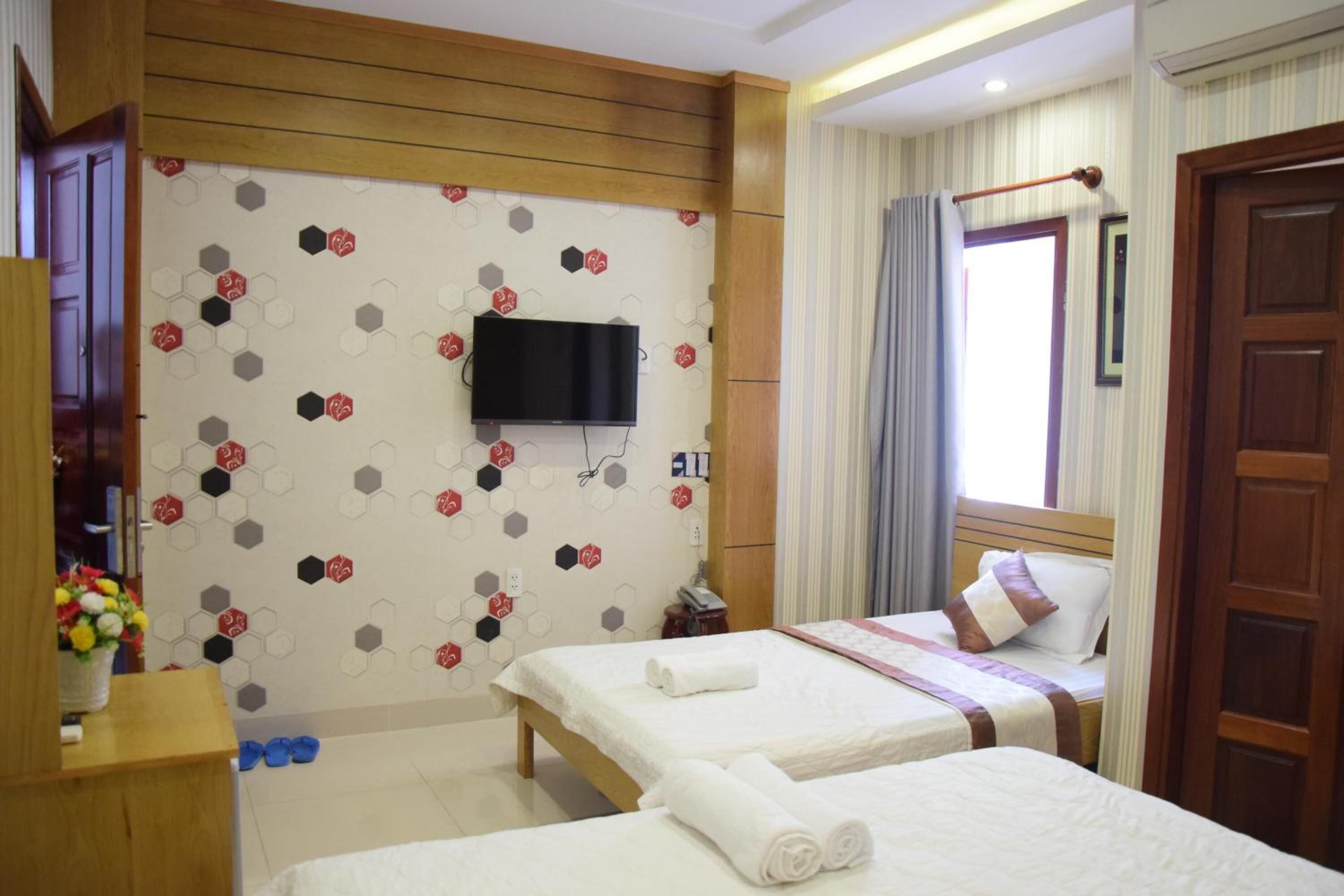 A hotel room with two beds, a TV mounted on the wall, a wooden wardrobe, and a window with curtains.