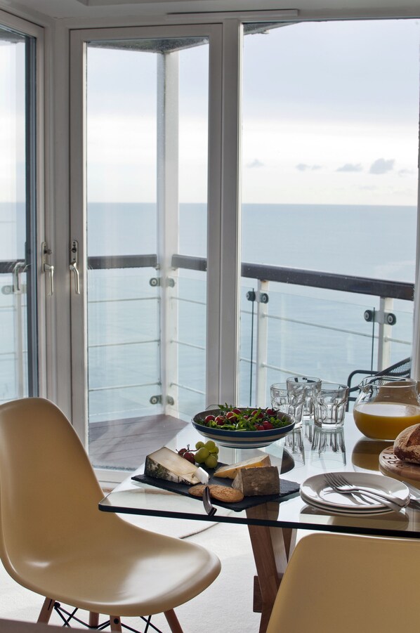 A balcony with a table set for dining, featuring a bowl of salad, cheese, and glasses.
