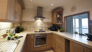A modern kitchen with wooden cabinets, stainless steel appliances, and a large window providing a view. - Marine Point, Mevagissey - sensational cliff top views of harbour and bay (Mevagissey)