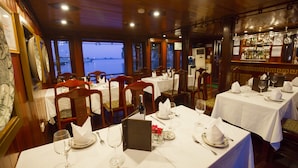 En restaurant med borde dækket til spisning, et barområde og udsigt til vandet.