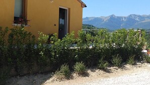 A yellow building with a door and window, surrounded by greenery and a view of mountains. - A modern independent apartment with a large private terrace. (Macerata)