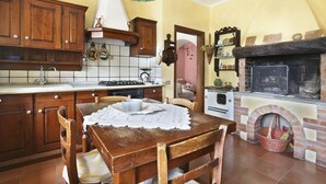 A traditional kitchen with wooden cabinets, a tiled backsplash, a dining table with chairs, a fireplace, and a hanging light fixture. - Chiantihouse near Florence (Montespertoli)
