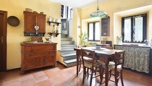 A kitchen with a wooden cabinet, a dining table with chairs, a staircase, and a window with lace curtains. - Chiantihouse near Florence (Montespertoli)