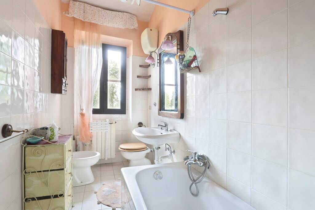 Casa de banho com banheira, sanita, lavatório e janela com cortinas.