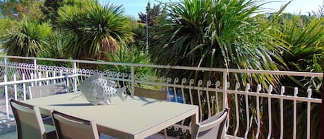 Un balcon agrémenté d’une table et de chaises, entouré d’une clôture blanche et d’une végétation luxuriante.
