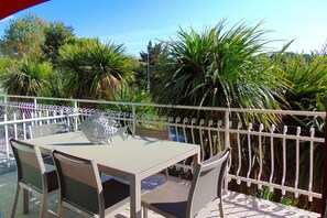 Un balcon agrémenté d’une table et de chaises, entouré d’une clôture blanche et d’une végétation luxuriante.