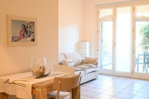 A dining area with a table, chairs, a glass with decorative items, a sofa, and a sliding glass door leading to an outdoor area. - S068 - Sirolo, new two-room apartment with terrace (Sirolo)