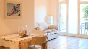Een eethoek met een tafel, stoelen, een glas met decoratieve objecten, een bank en een glazen schuifdeur naar een buitenruimte.