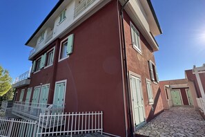 A two-story building with a red facade, white balcony railings, and green shutters. - S068 - Sirolo, new two-room apartment with terrace (Sirolo)
