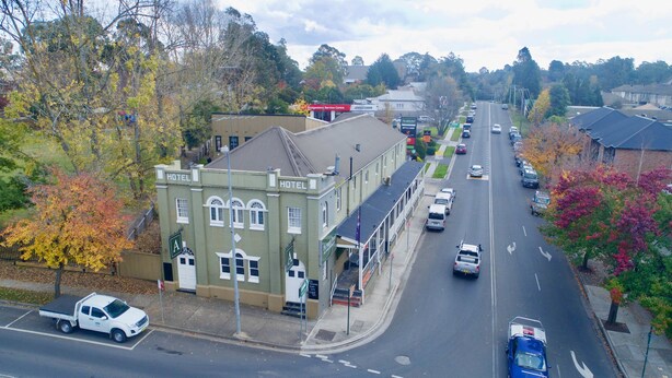 A hotel with a green facade, a corner location, and a street view with cars and trees. - Argyle Hotel Southern Highlands (Moss Vale)