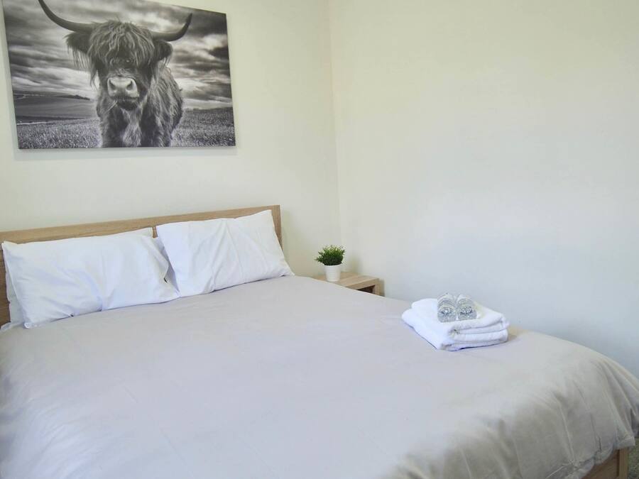 Una cama bien tendida con ropa de cama blanca, una mesita de noche con una planta y una obra de arte en la pared de un toro.