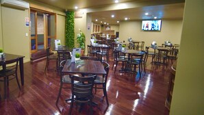 A restaurant with wooden tables and chairs, a TV screen, and a green wall. - Argyle Hotel Southern Highlands (Moss Vale)