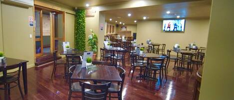 Un restaurante con mesas y sillas de madera, una pantalla de televisión y una pared verde.