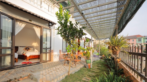 A hotel room with a bed, a small table, and a chair. There is a covered outdoor area with plants and a fence. - Sen Da Villa - Succulent Villa (Xuan Huong - Da Lat)
