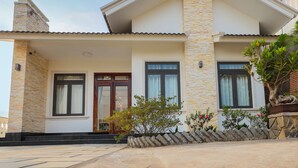 A two-story house with a stone facade, a front porch, and a small garden with a cactus and flowering plants. - Sen Da Villa - Succulent Villa (Xuan Huong - Da Lat)