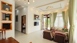 A spacious living area with a dining table, a sofa set, and a television. There are framed pictures on the wall and a window with curtains. - Sen Da Villa - Succulent Villa (Xuan Huong - Da Lat)
