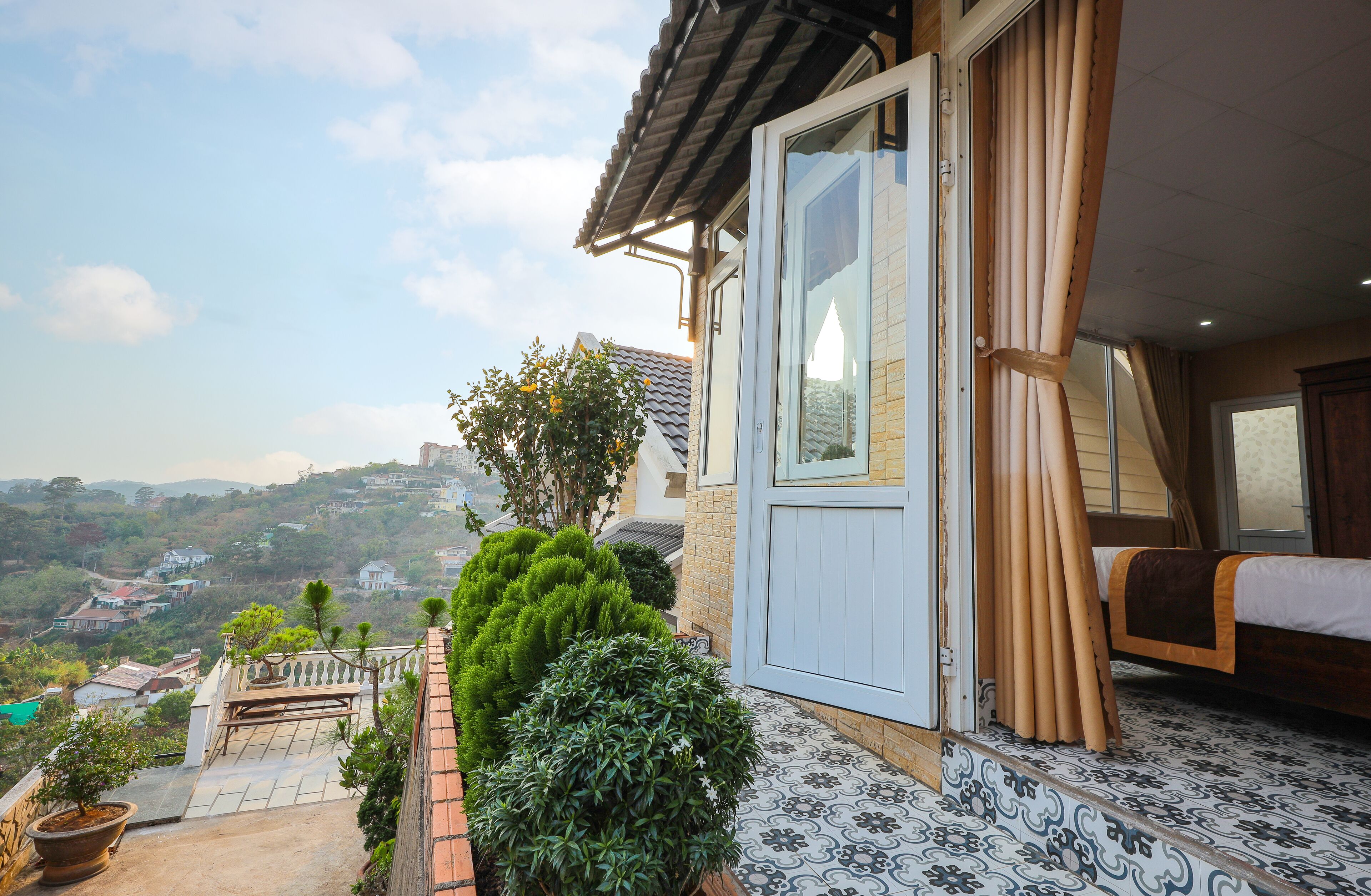 A room with a bed, a window with curtains, and a view of a hilly landscape.