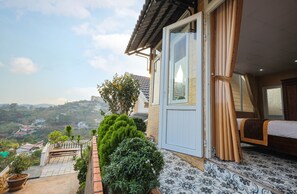 A room with a bed, a window with curtains, and a view of a hilly landscape. - Sen Da Villa - Succulent Villa (Xuan Huong - Da Lat)