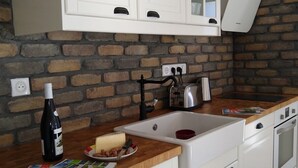 A kitchen with white cabinets, a brick wall, a wooden countertop, a sink, a stove, and a wine bottle. - MODERN DUPLEX APARTMENT? CENTRAL LOCATION - SLEEPS 5 (Le Bourg-d'Oisans)