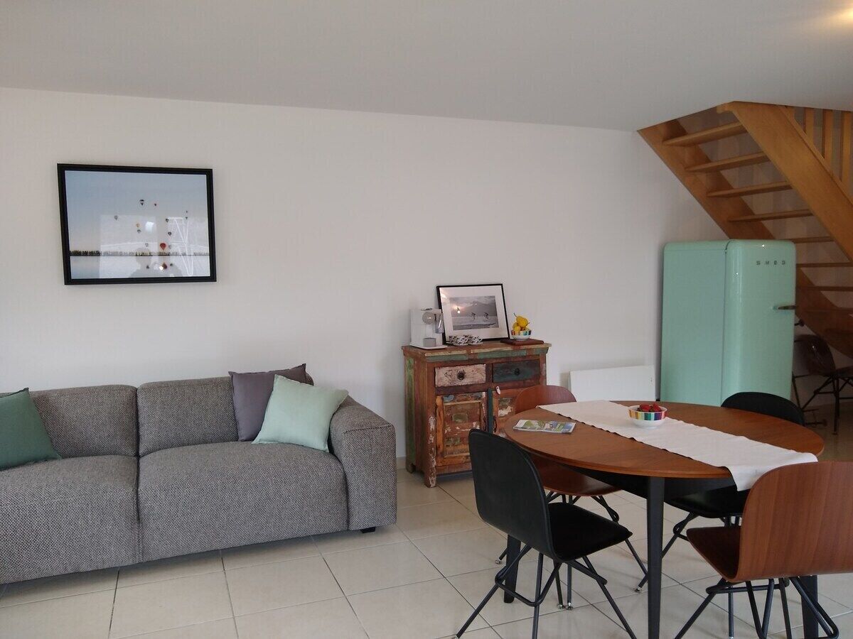 Una sala de estar con sofá, un aparador de madera, una mesa de comedor con sillas y una escalera.