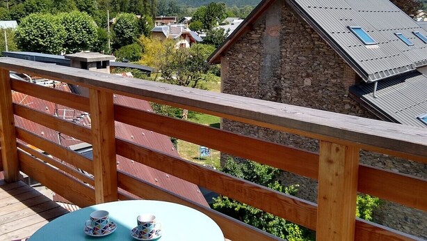A wooden deck with a table and chairs, overlooking a mountain and a small stone building. - MODERN DUPLEX APARTMENT? CENTRAL LOCATION - SLEEPS 5 (Le Bourg-d'Oisans)