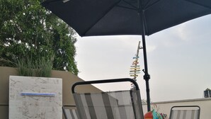 Un patio con mobiliario exterior, incluyendo sillas y una mesa, bajo un paraguas grande.