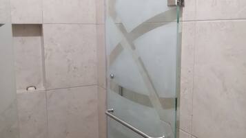 Cabina de ducha con paredes de azulejos, una barra de apoyo metálica y desagüe visible, todo ello envuelto en cristal.