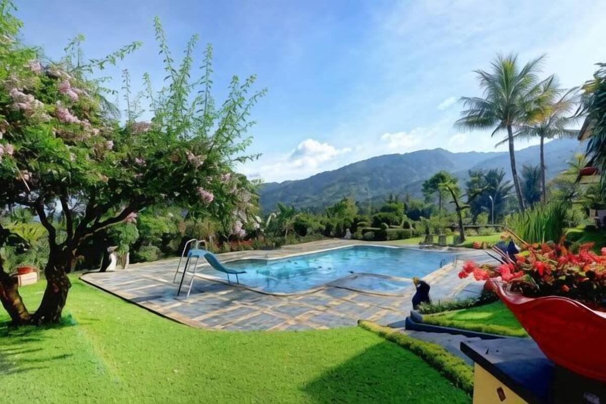 Ein Swimmingpool mit Rutsche, umgeben von gepflegtem Rasen und Bäumen, mit Bergen im Hintergrund.