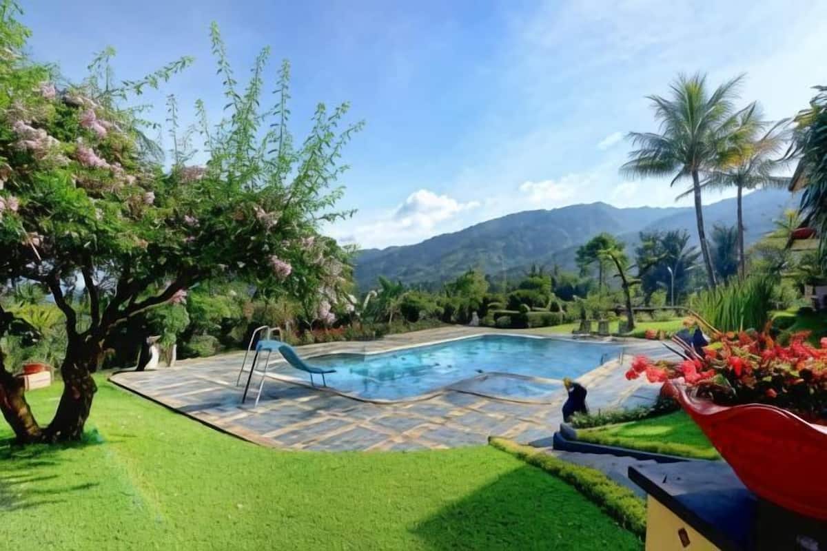 A swimming pool with a slide, surrounded by well-maintained grass and trees, with mountains in the background.