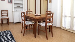 A dining area with a wooden table and chairs, a white cabinet, and a bed with a patterned bedspread. - M152 - Marcelli, new three-room apartment with garden (Marcelli)