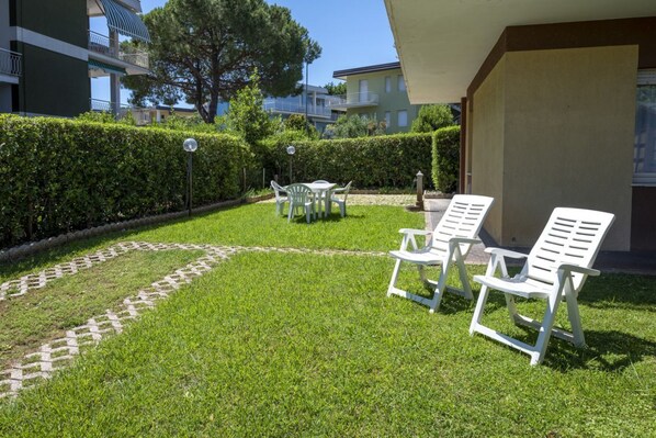 A well-maintained outdoor area with a lawn, a small table with chairs, and two lounge chairs.