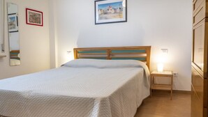 A bedroom with a bed, bedside table, wall-mounted light, and a painting. - M152 - Marcelli, new three-room apartment with garden (Marcelli)