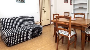 A room with a patterned sofa, wooden dining table, chairs, and a white bookshelf. - M152 - Marcelli, new three-room apartment with garden (Marcelli)