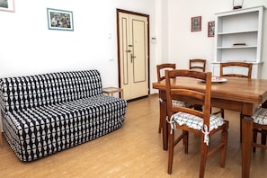 A room with a patterned sofa, wooden dining table, chairs, and a white bookshelf.