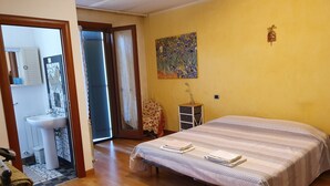 Ein Schlafzimmer mit Bett, Nachttisch, Sessel, einem Gemälde und einem durchgegangenen Tür sichtbaren Badezimmer.