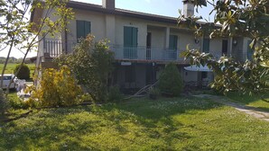 Ein zweistöckiges Gebäude mit Balkon, umgeben von Grünpflanzen und einem gepflasterten Auffahrt.