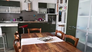Ein Holzespeisesaal mit Stühlen, ein Küchenbereich mit Schränken und Geräten sowie ein gefliester Boden.