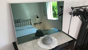 Et soveværelse med et stort spejl, en seng, et lille bord med en lampe og et tøjstativ.