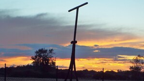 A fence with a metal gate and a large cylindrical object, possibly a barrel, in a grassy area during sunset. - 3 Bedroom historic house in Norfolk (Thetford)