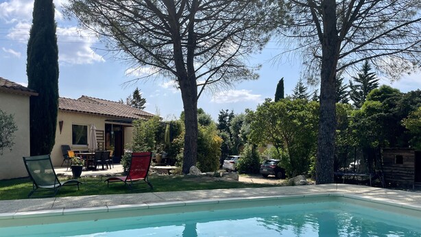 A swimming pool with a patio area, a dining table, and chairs.