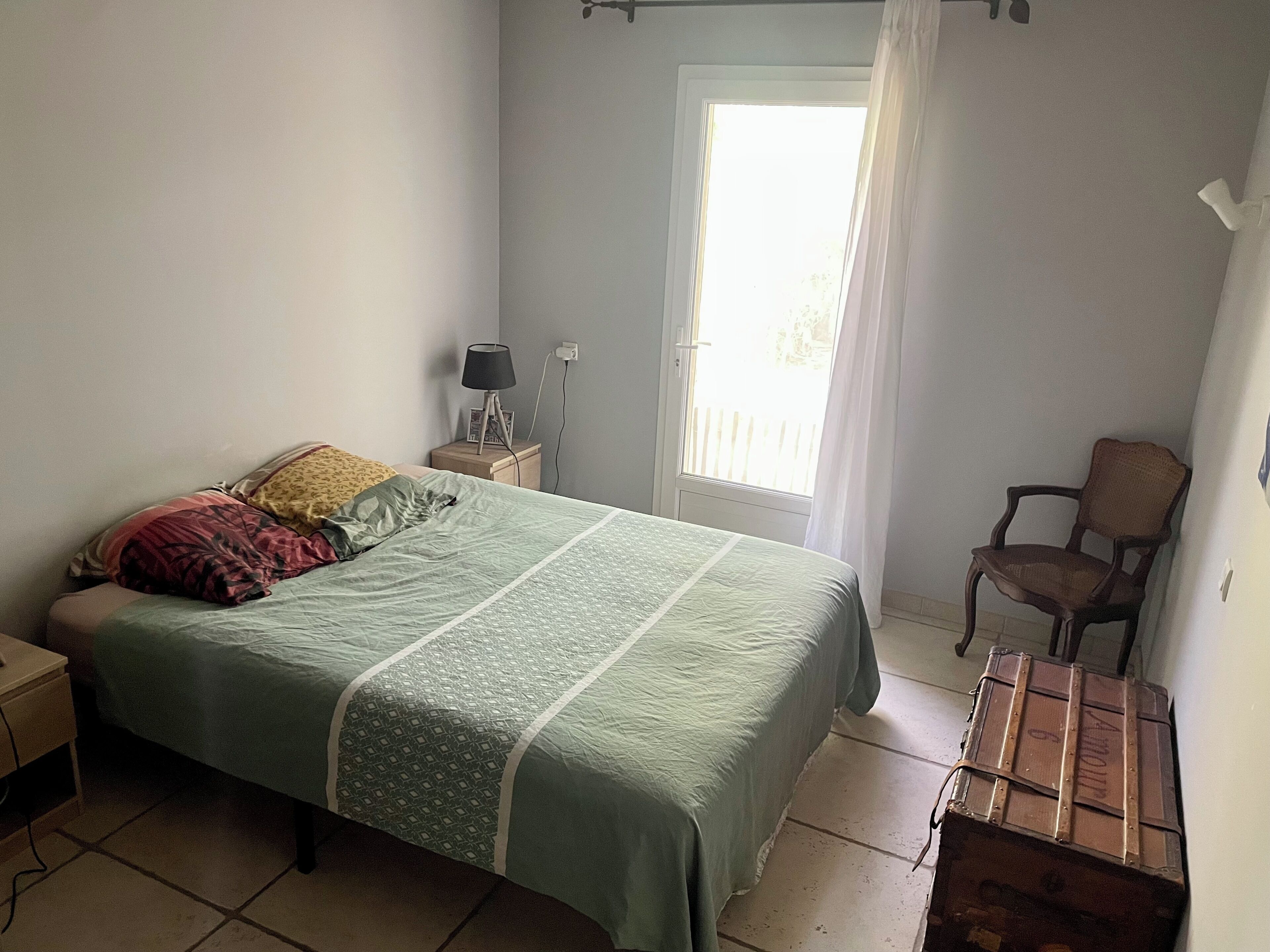 Un dormitorio con cama, mesita de noche, lámpara, silla y maleta.