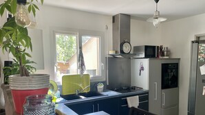A modern kitchen with a sink, stove, and microwave. There is a window providing natural light and a plant on the counter.
