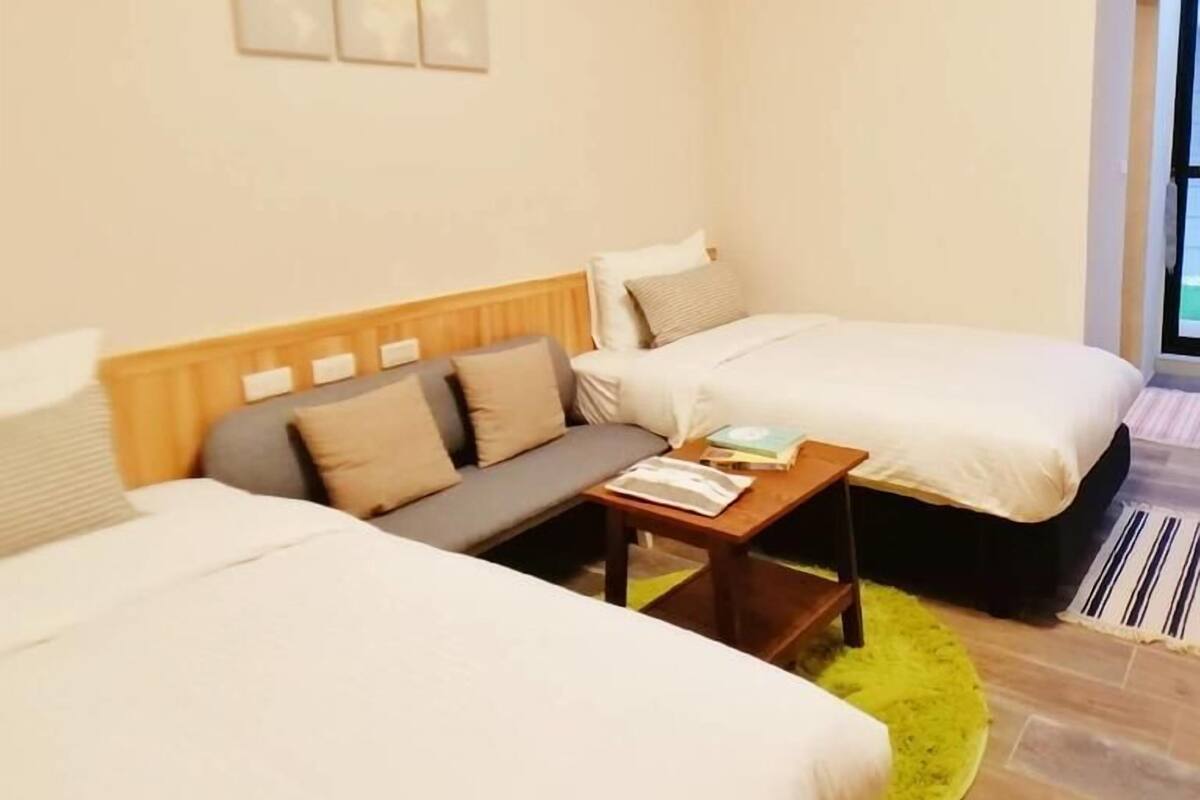A hotel room with two beds, a sofa, a small table, and a bright yellow rug.