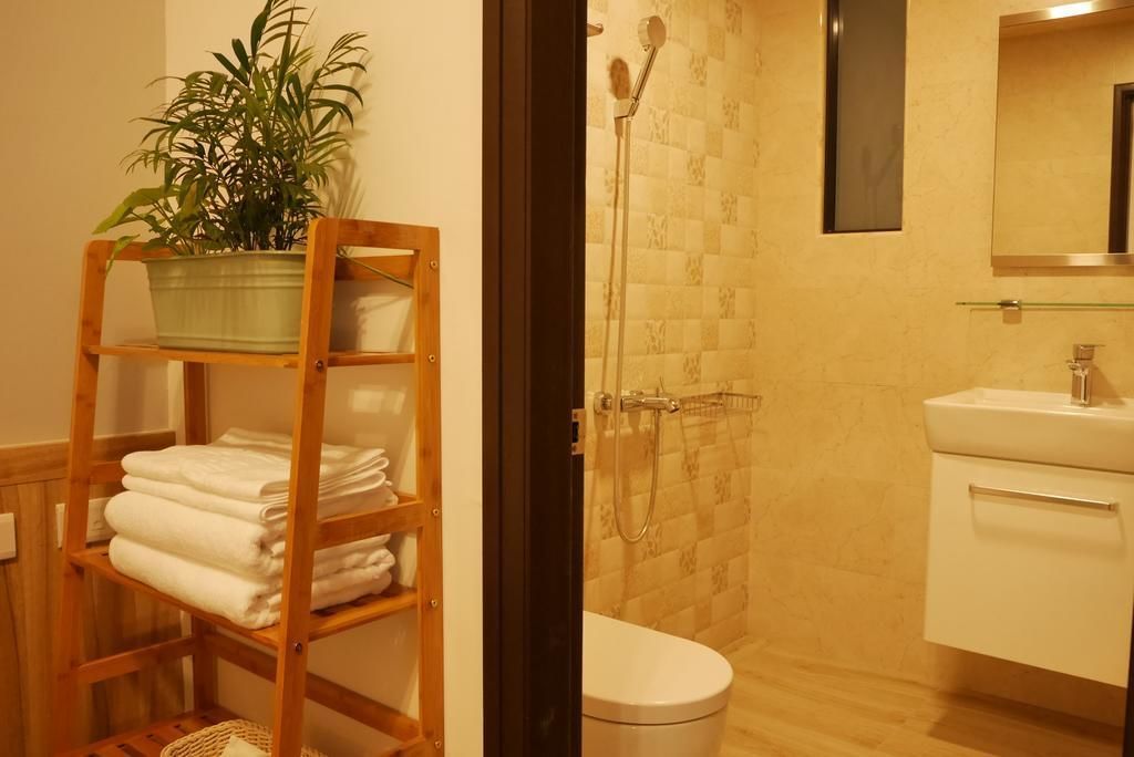 A bathroom with a shower, toilet, and sink. There is a wooden shelf with towels and a potted plant.