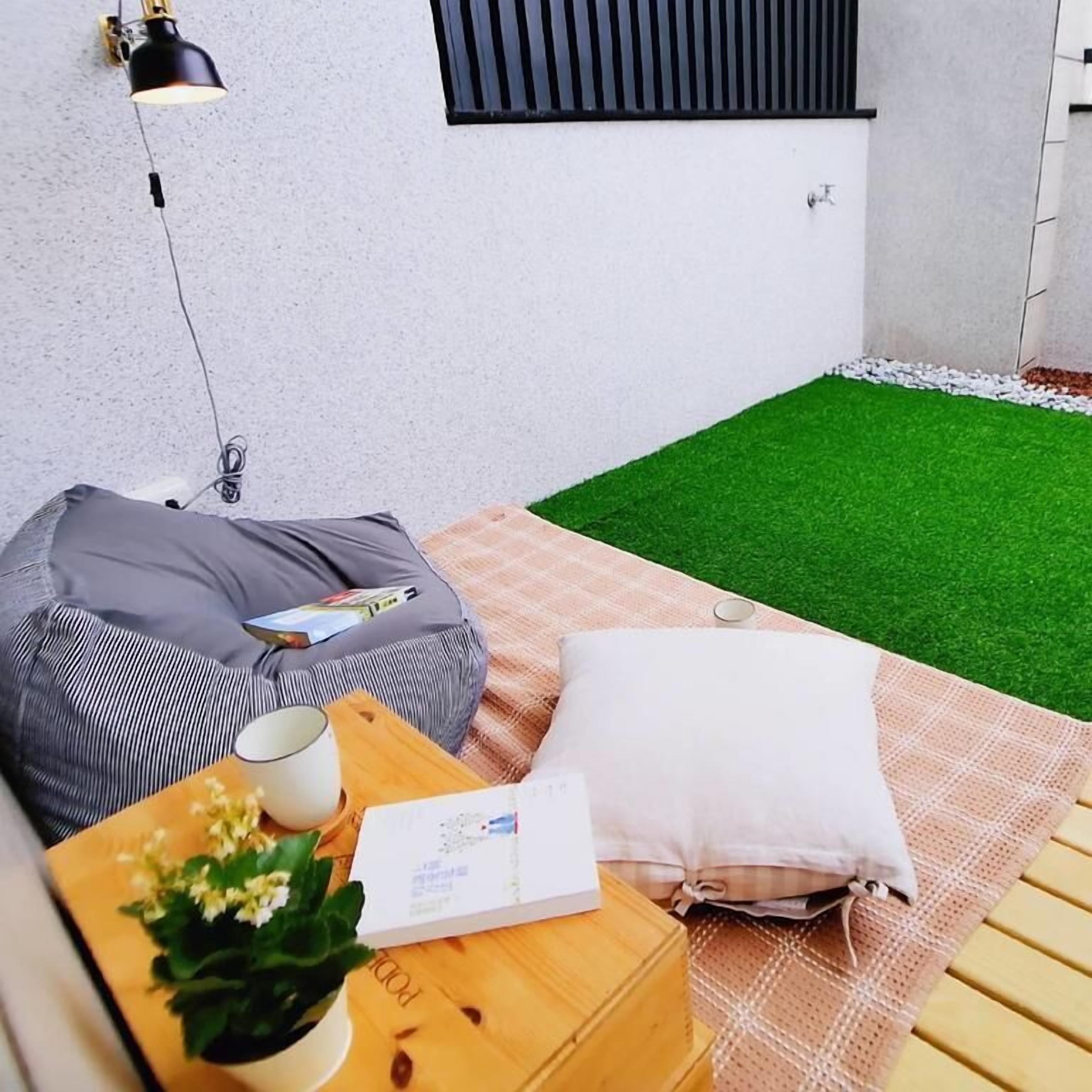 A small outdoor seating area with a wooden table, a cushion, a pillow, and a small plant.