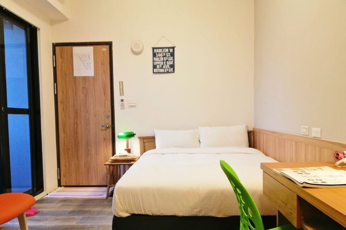 A bedroom with a bed, a desk, a chair, a door, and a wall sign.