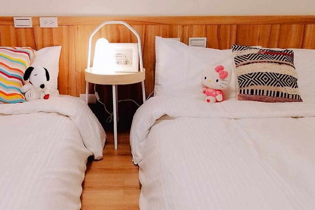 A hotel room with two beds, each with a distinct pillow design. A small table with a light is placed between the beds.