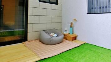 Quarto moderno com porta de vidro, poltrona de tecido cinza, uma mesinha com um vaso e um tapete xadrez.